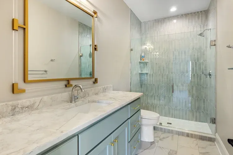 Bright marble bathroom with gold-framed mirror, mint vanity, and frosted glass shower