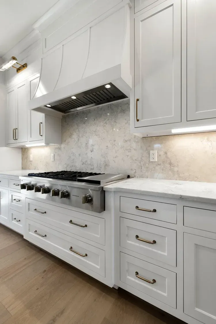 Bright white kitchen with a large stainless steel range, marble backsplash, and paneled cabinets