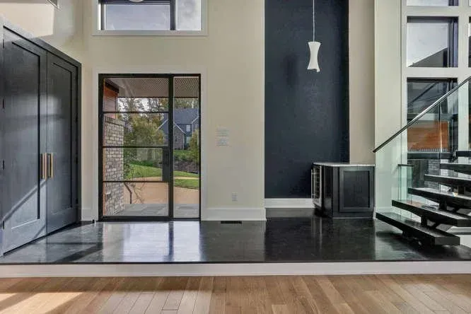 Modern living room with black staircase, tall windows, glass doors, and dark accent wall
