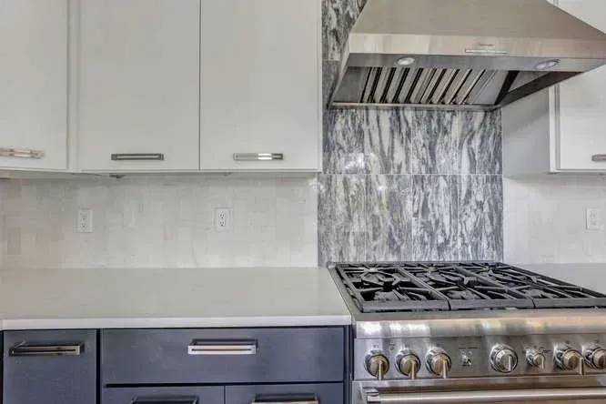 Modern kitchen with white cabinets, marble backsplash, stainless steel range, and gray countertop