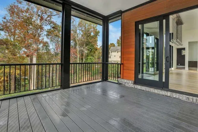 Covered deck with gray flooring, black railing, and glass doors overlooking trees