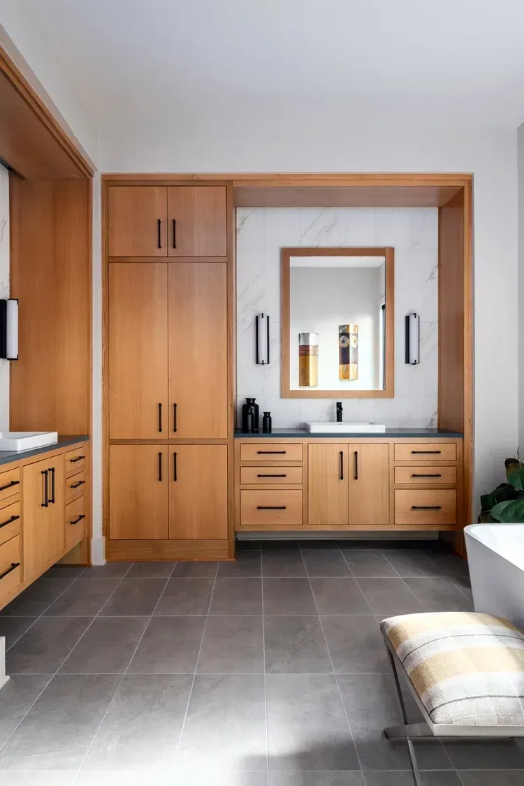 Built-in wooden bathroom vanity with mirror, cabinets, and dark tile floor in a modern room