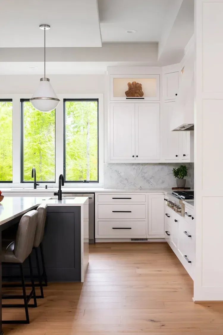 Bright modern kitchen with white cabinets, black window frames, wood floors, and a black island.