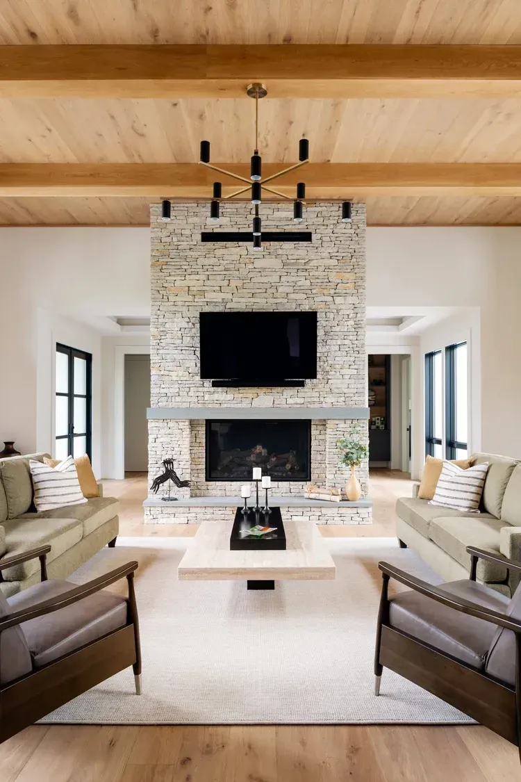 Bright living room with a stone fireplace, large TV, white sofas, and a wood-beamed ceiling