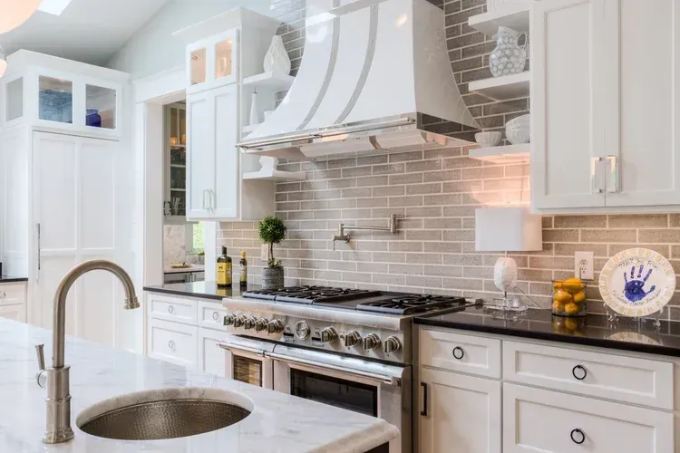 Bright white kitchen with marble island, stainless stove, and light gray subway tile backsplash