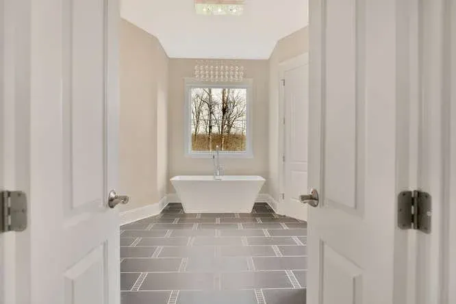 Bright bathroom with double doors, gray tile floor, and a freestanding tub by a window.