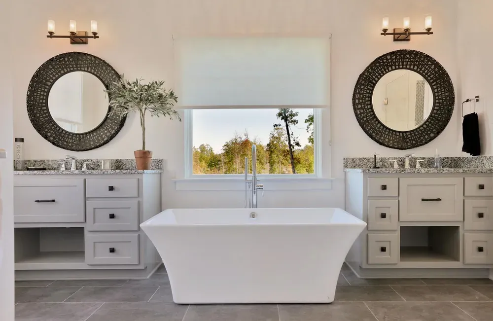 Modern bathroom with freestanding tub, double vanities, round mirrors, and a window view of trees