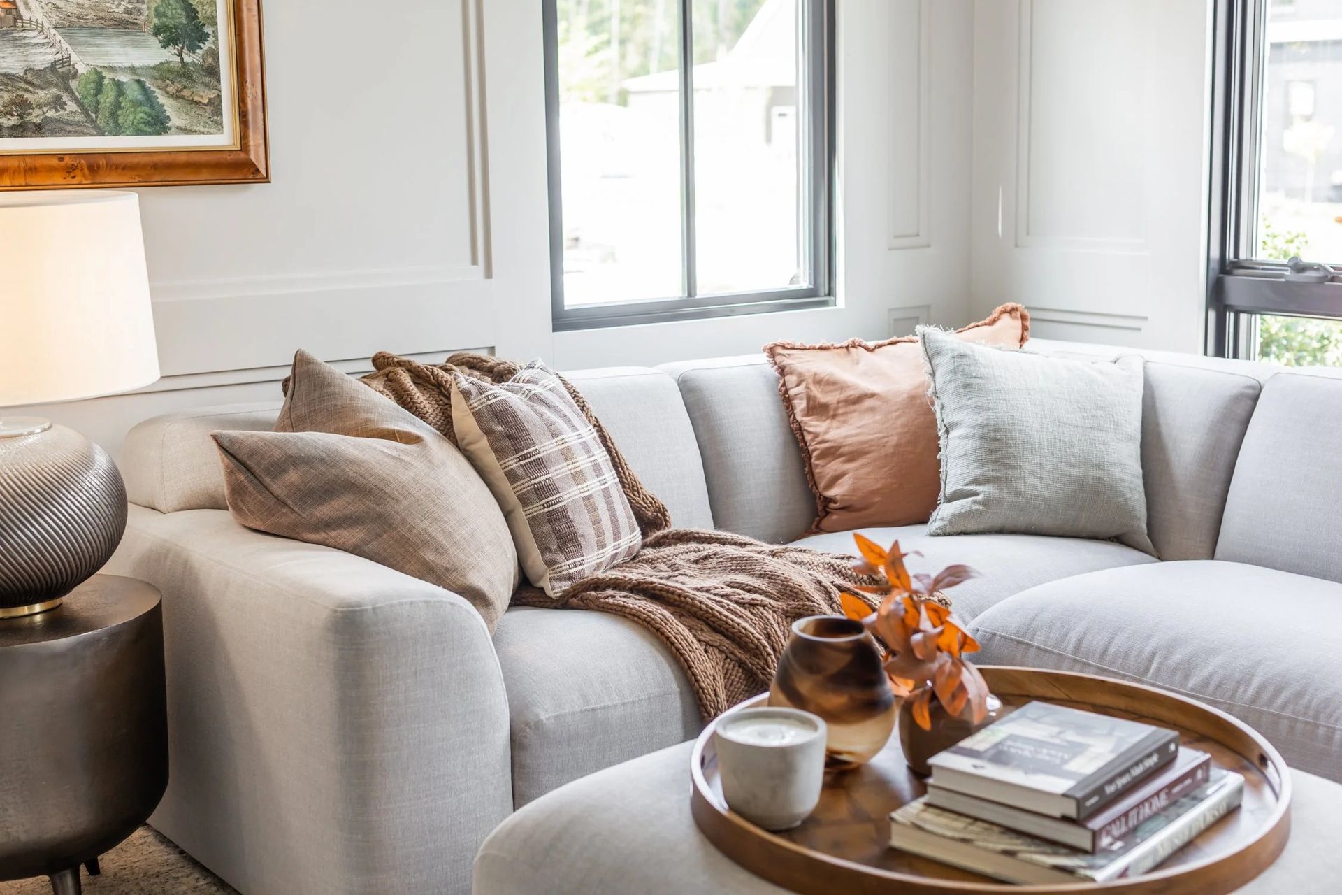 A light gray sectional sofa with assorted throw pillows, a knit blanket, and a round wooden coffee table with books.