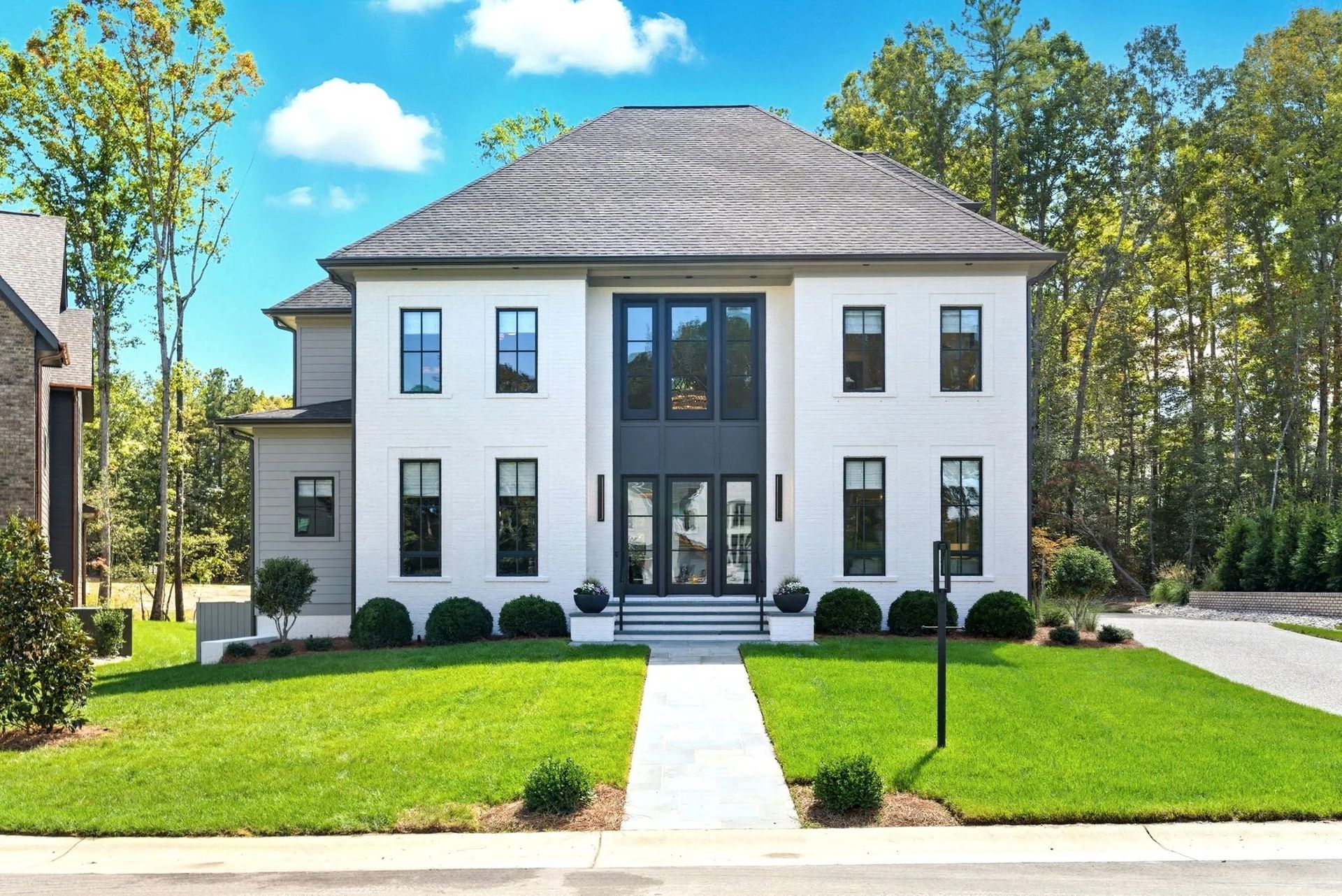 A two-story white brick house with a dark roof and black-framed windows, featuring a central entry and a green lawn.