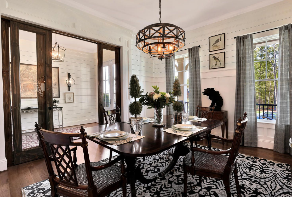 A formal dining room features a dark wood table with matching chairs on a patterned rug under a rustic chandelier.