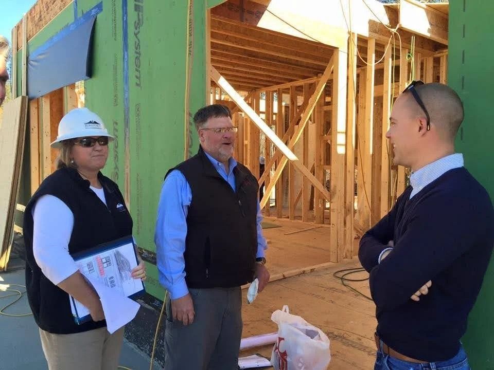 Three professionals discuss a building project at an active construction site with wooden framing.