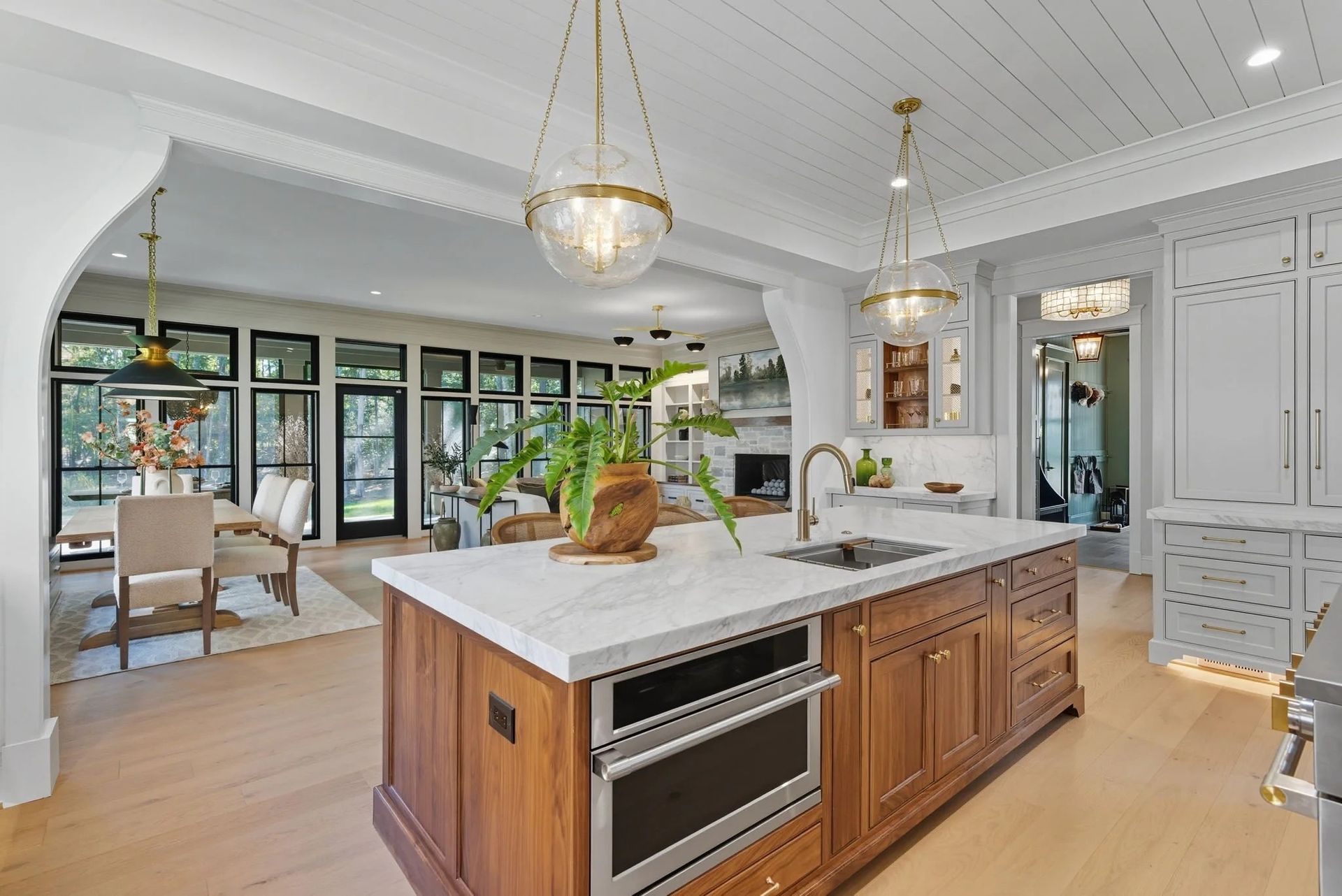 A kitchen island with a marble countertop and wood cabinets in a bright, open-plan home featuring a dining area beyond.