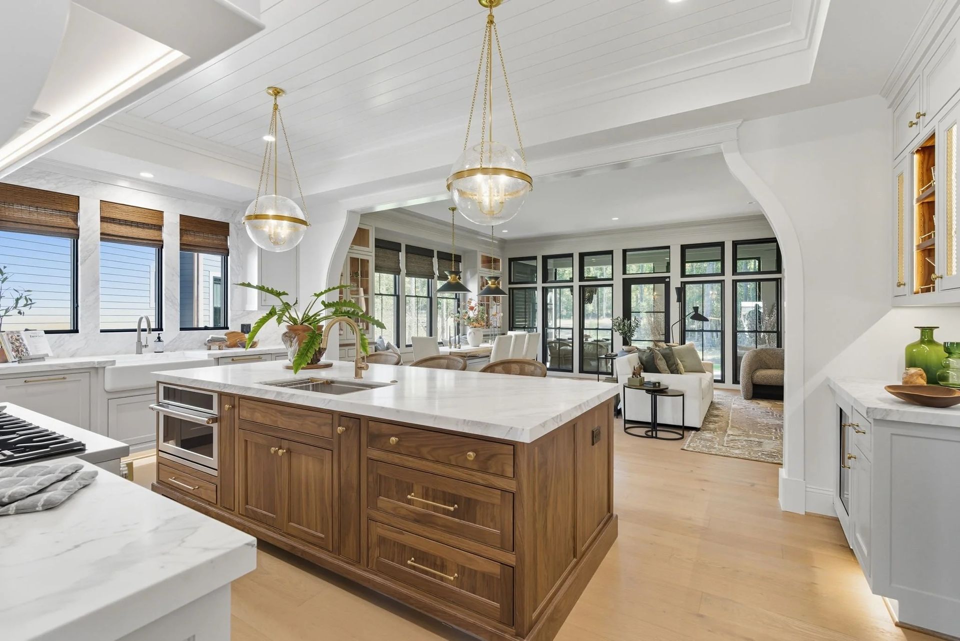 A luxury kitchen featuring a large wooden island with a marble countertop, brass lighting, and a view into a living area.
