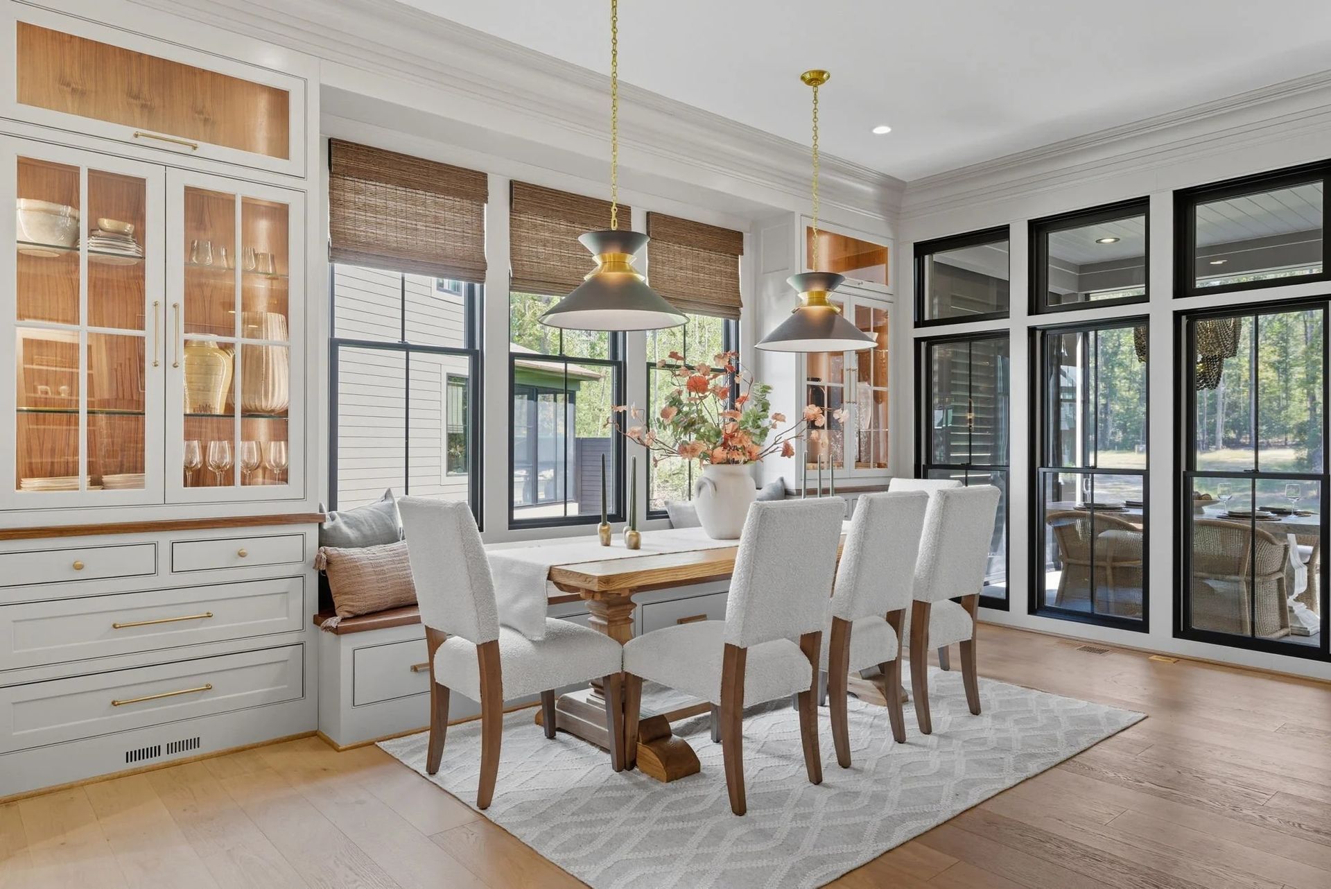A bright dining nook features a wooden table with white chairs, a built-in cabinet, bench seating, and two pendant lights.