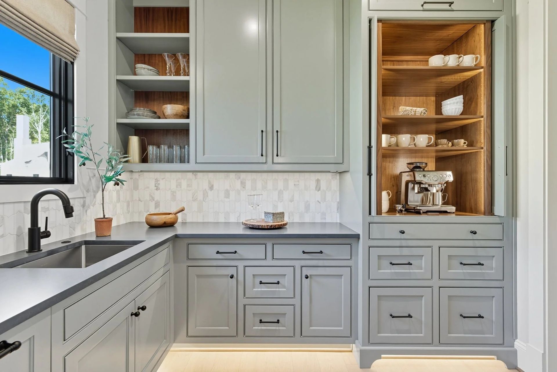 A gray kitchen featuring a sink, open shelving, cabinetry, and a dedicated coffee station inside a tall cabinet.