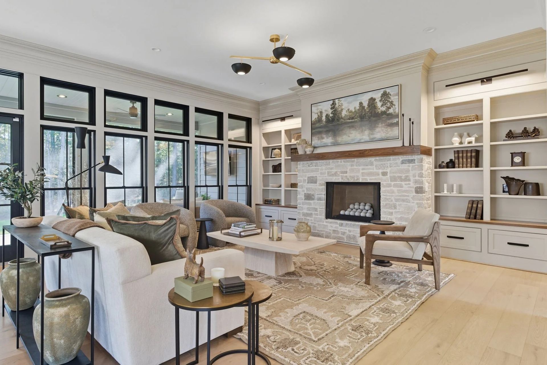 A bright, modern living room featuring white built-in bookshelves, a stone fireplace, and a neutral-toned sofa set.