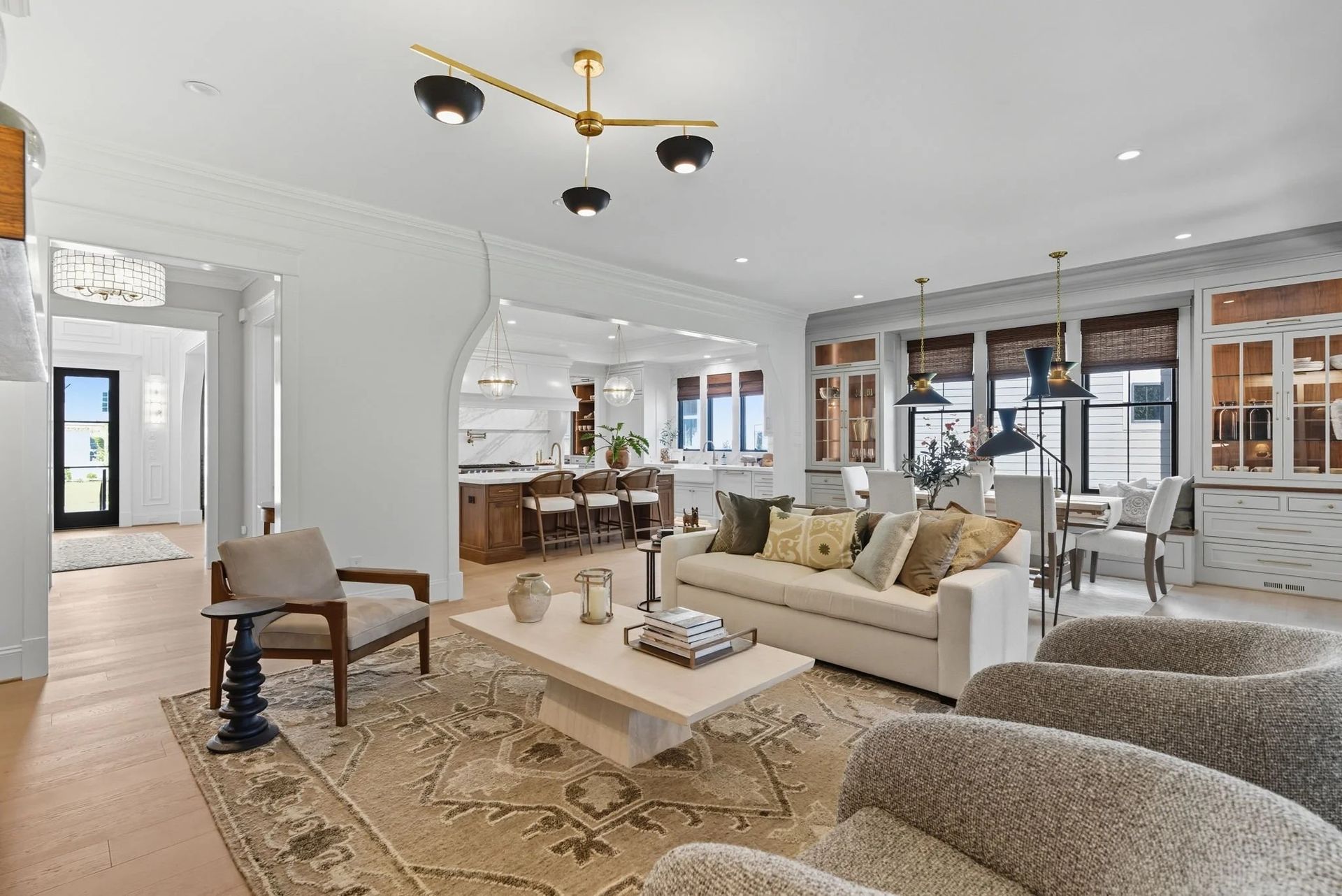 A bright, modern open-plan living and dining area featuring neutral furniture, hardwood floors, and a kitchen in the rear.