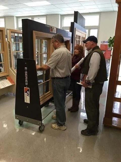Three people in a showroom examine a window display mounted on a rolling frame.