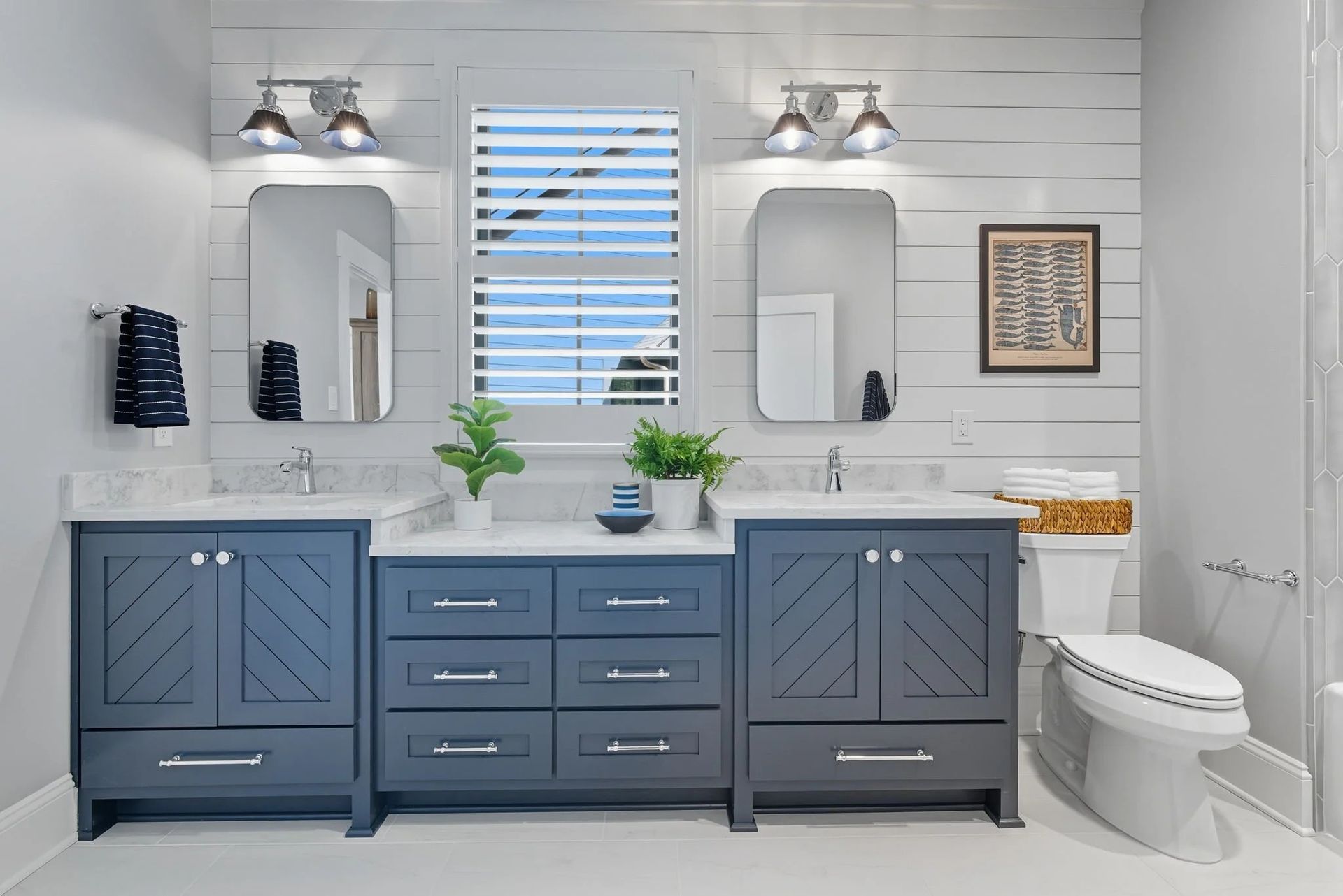 A modern bathroom with two dark gray vanities, white countertops, dual mirrors, farmhouse lighting, and white shiplap walls.