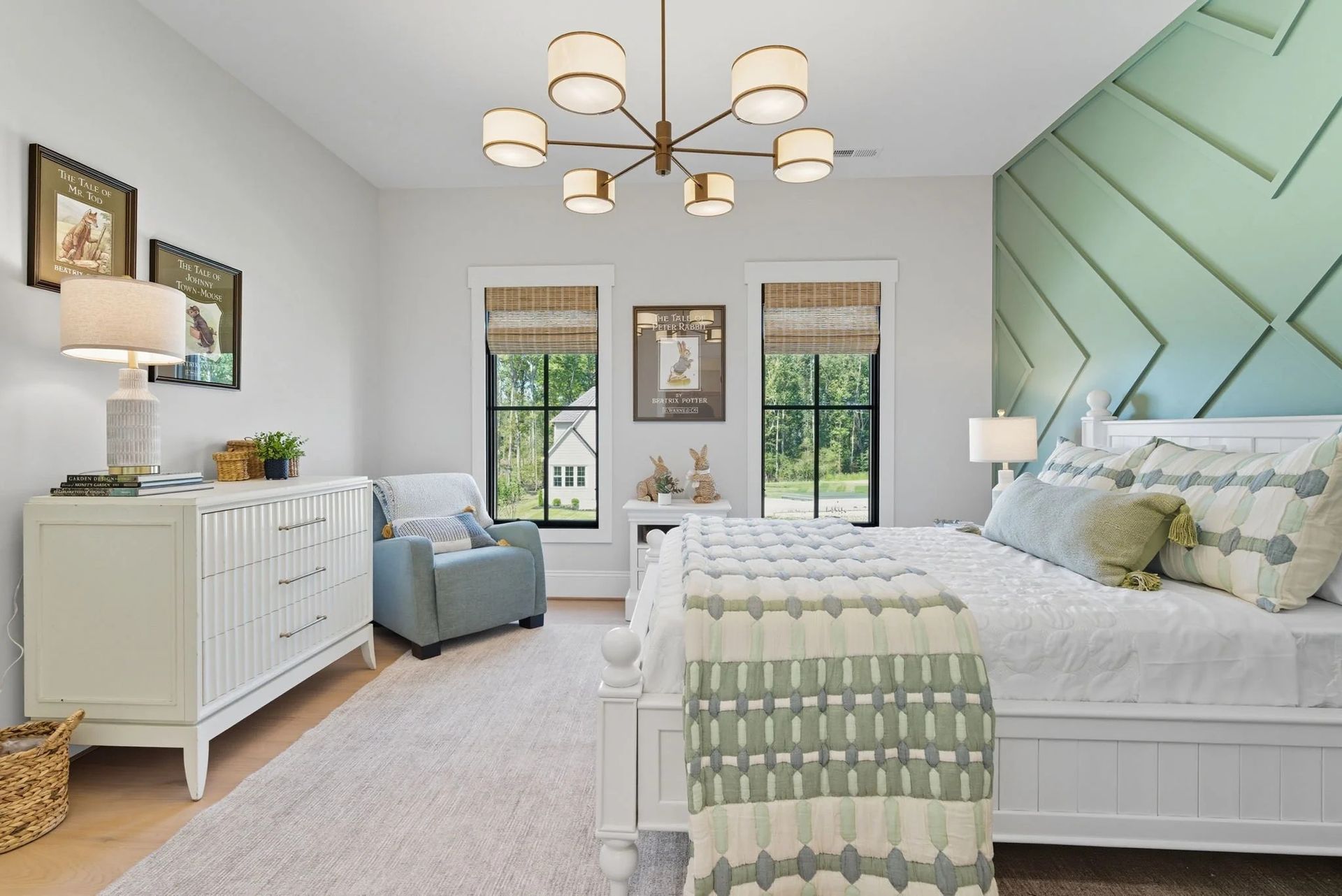 A bright bedroom with a white dresser, a blue armchair, a bed with light green bedding, and a geometric green accent wall.