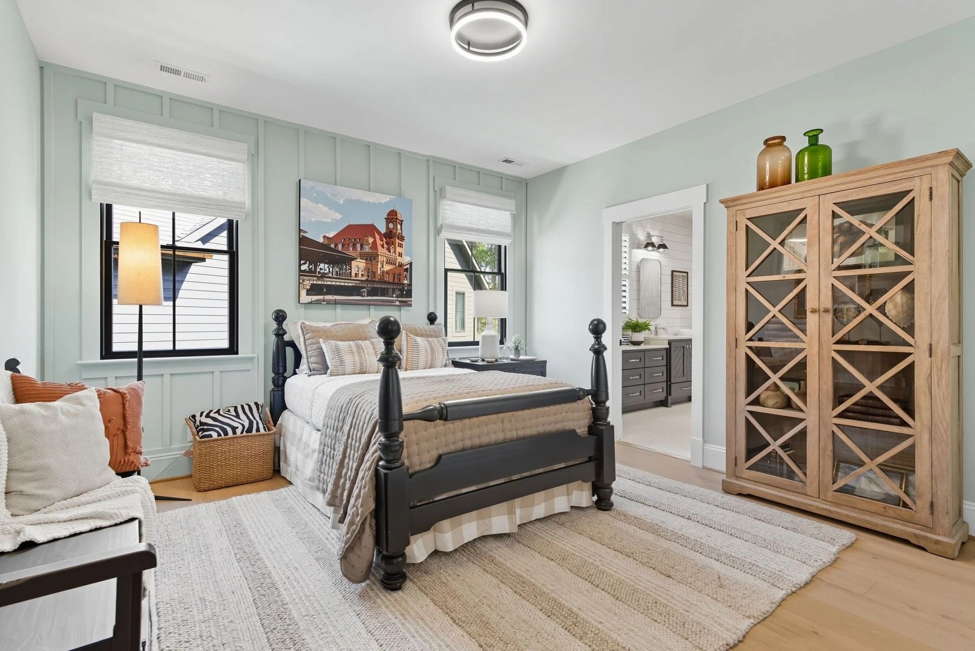 A modern bedroom featuring a black four-poster bed, light blue paneled walls, a large wooden cabinet, and a textured rug.