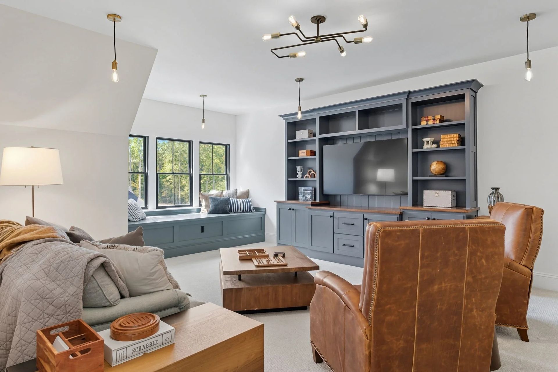 A cozy, bright living room features a blue built-in media center, leather armchairs, and a window seat with cushions.