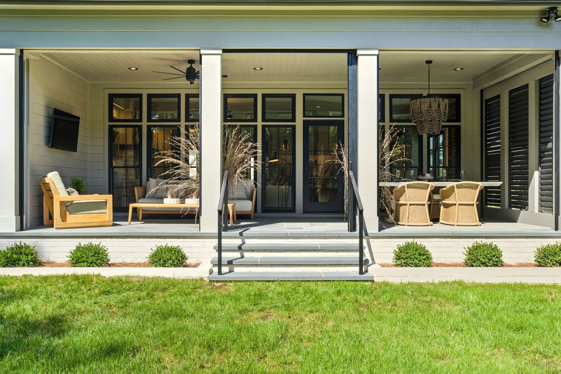 A covered outdoor patio featuring a seating area, a dining set, and central stairs leading to a green lawn.