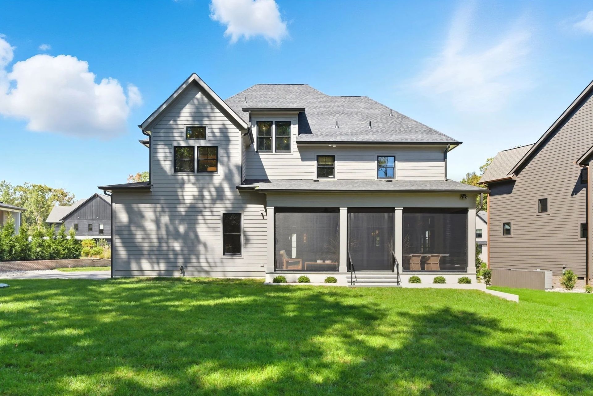 A gray two-story house with a screened-in back porch, large lawn, and a bright blue sky with clouds.