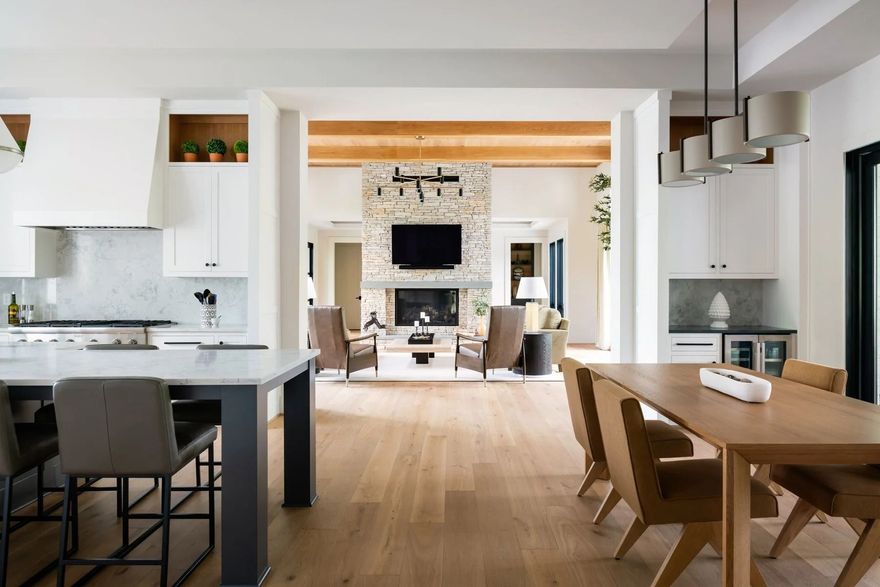 A bright, open-concept home interior featuring a white kitchen, a dining area with a wooden table, and a cozy living room.