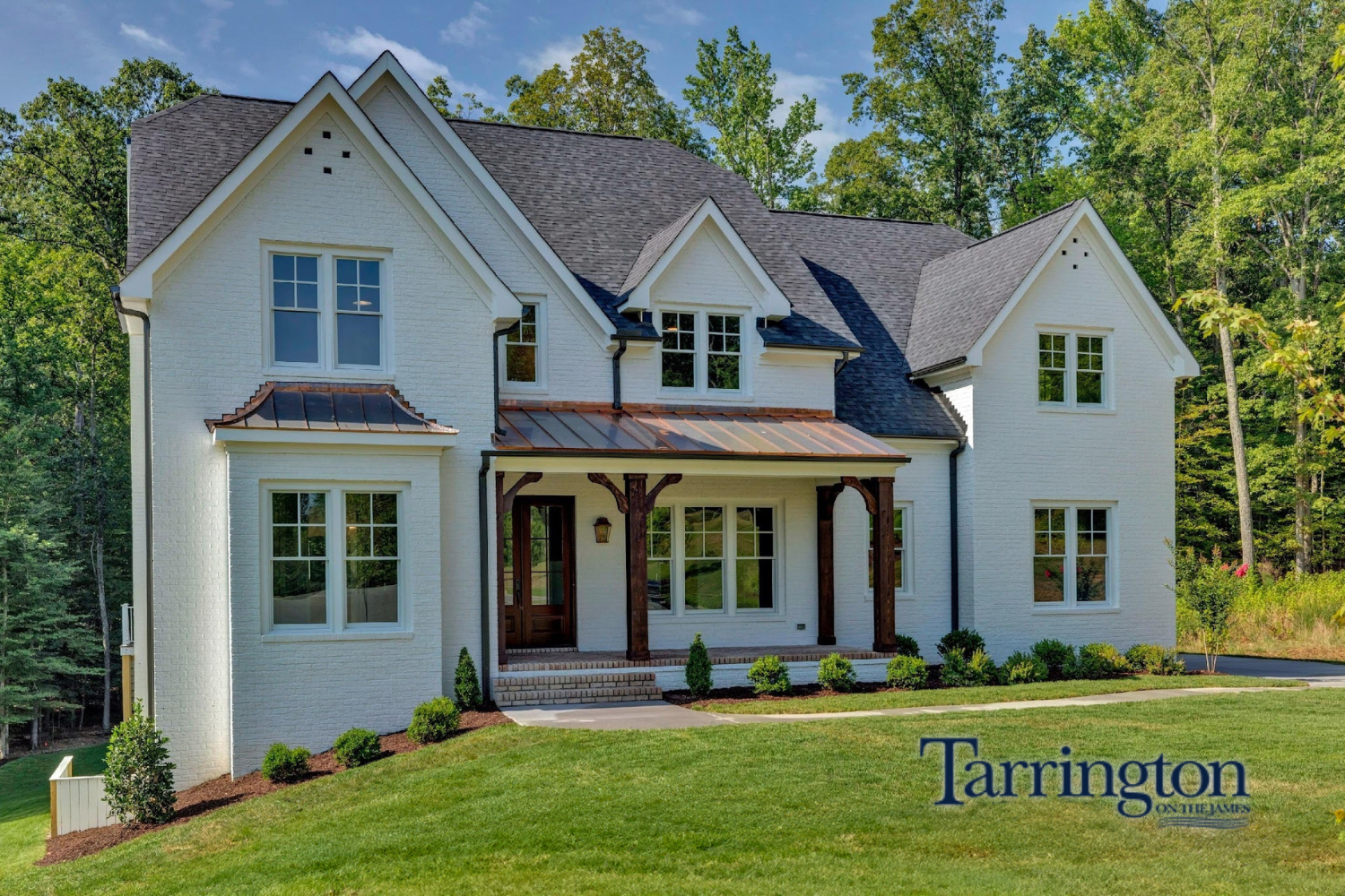 A two-story white brick house with a dark shingled roof, copper porch accents, and wooden posts, set against a forest.