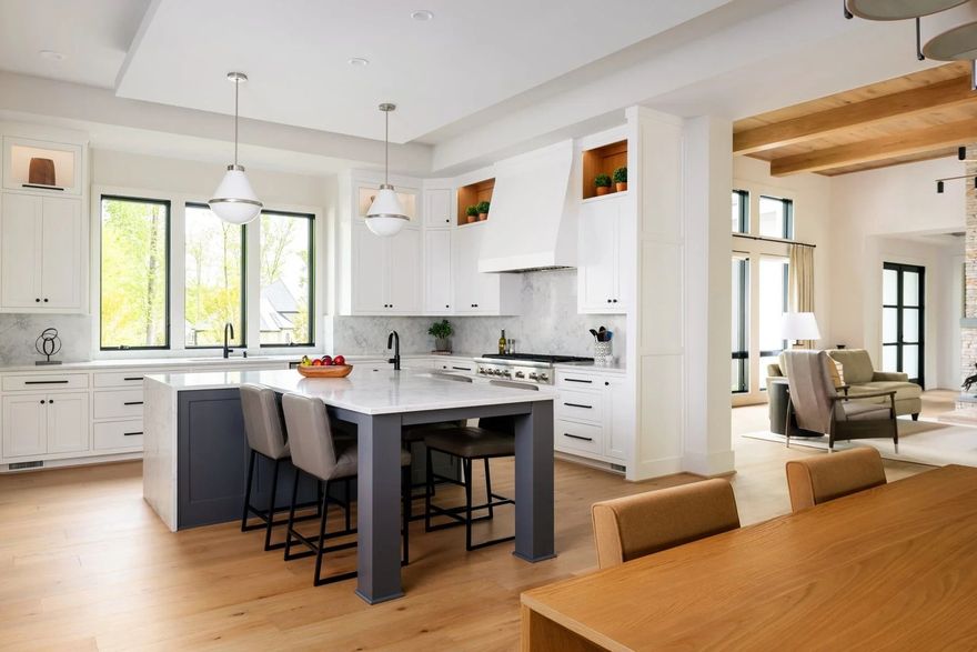 A bright, open-plan kitchen featuring white cabinets, a large grey island with stools, and wooden floors.