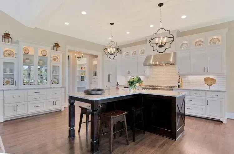 Bright white kitchen with dark island, pendant lights, and glass-front cabinets