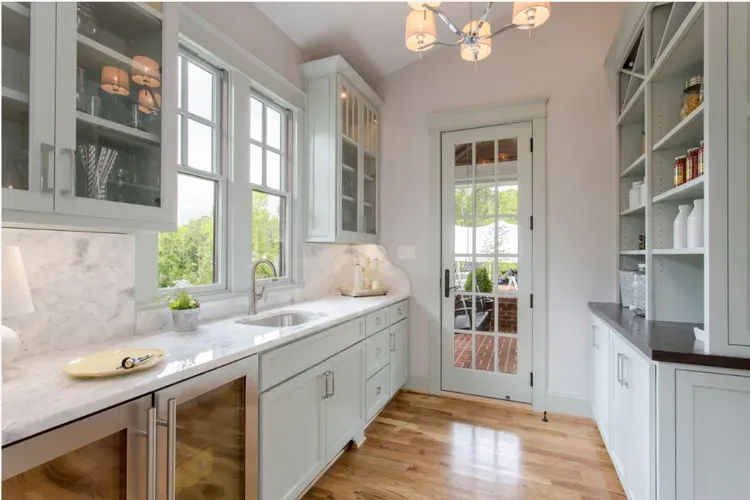 Bright white galley kitchen with marble counters, gray cabinets, wood floor, and glass-paned door.