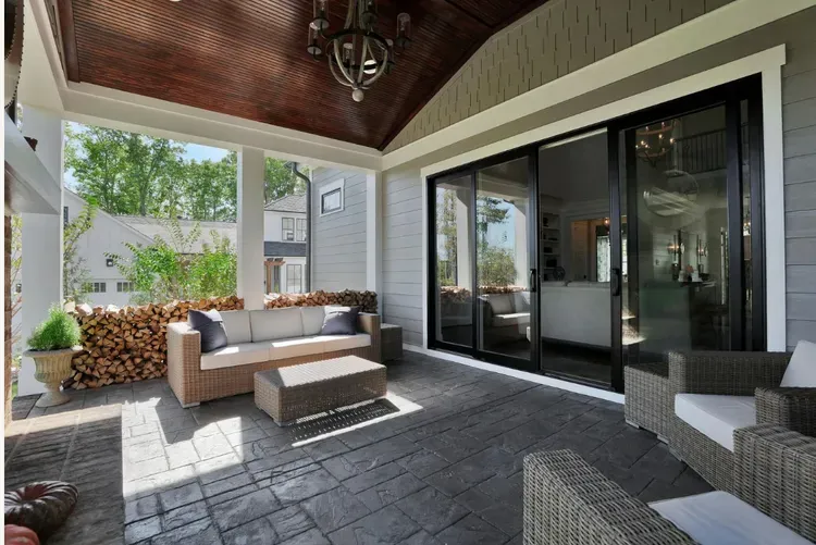 Covered patio with wicker seating, a low coffee table, and sliding glass doors overlooking a backyard.