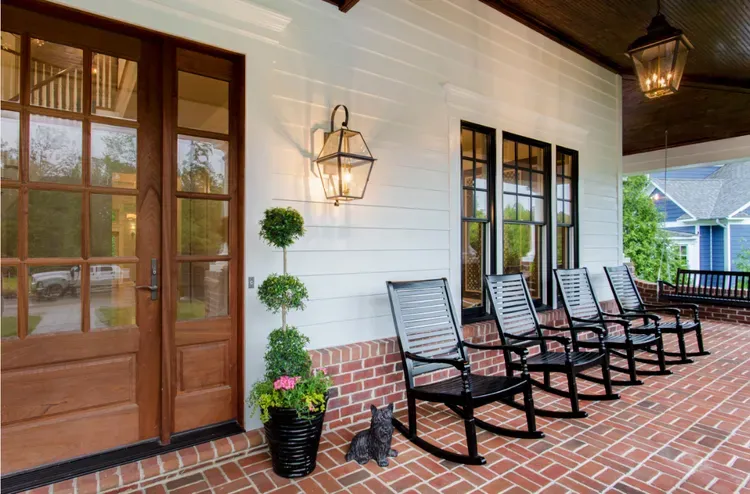 Brick porch with wooden double doors, black chairs, and potted plants under a covered entryway