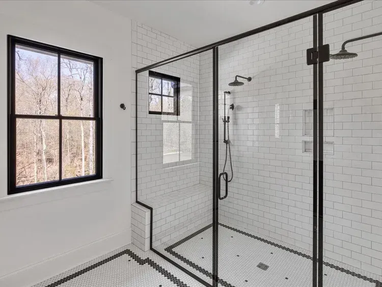Modern white bathroom with black-framed shower, glass doors, and window beside it