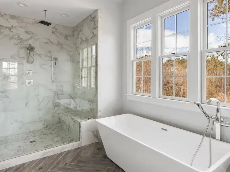 Modern bathroom with marble shower, freestanding tub, and large windows overlooking trees
