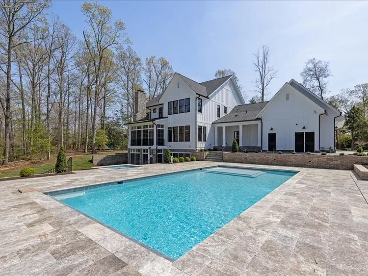 Backyard with a turquoise swimming pool beside a white house and detached garage