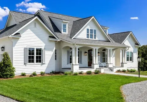 White suburban house with gray roof, front porch, and green lawn under a blue sky