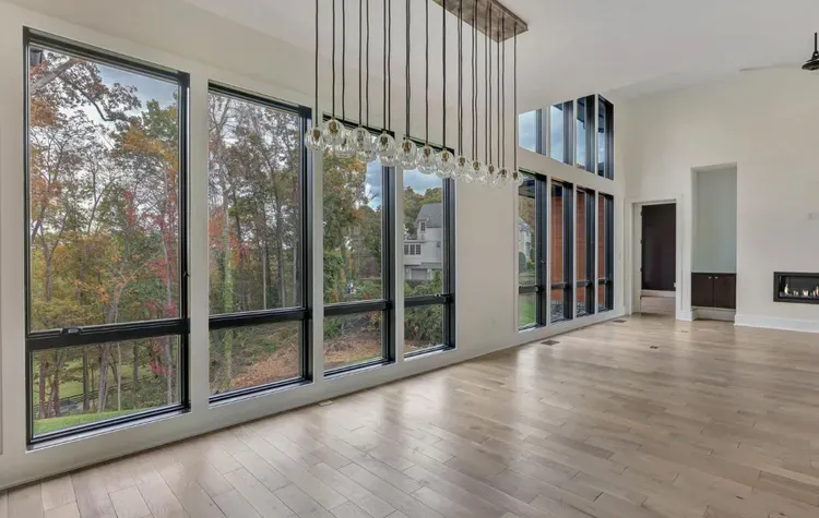 Modern empty living room with floor-to-ceiling windows, wood floors, and hanging pendant lights