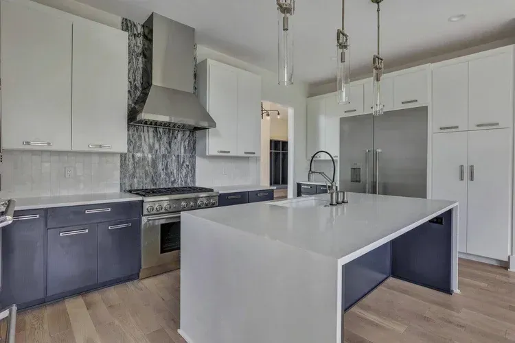 Modern white kitchen with gray cabinets, stainless appliances, and a large island with sink.