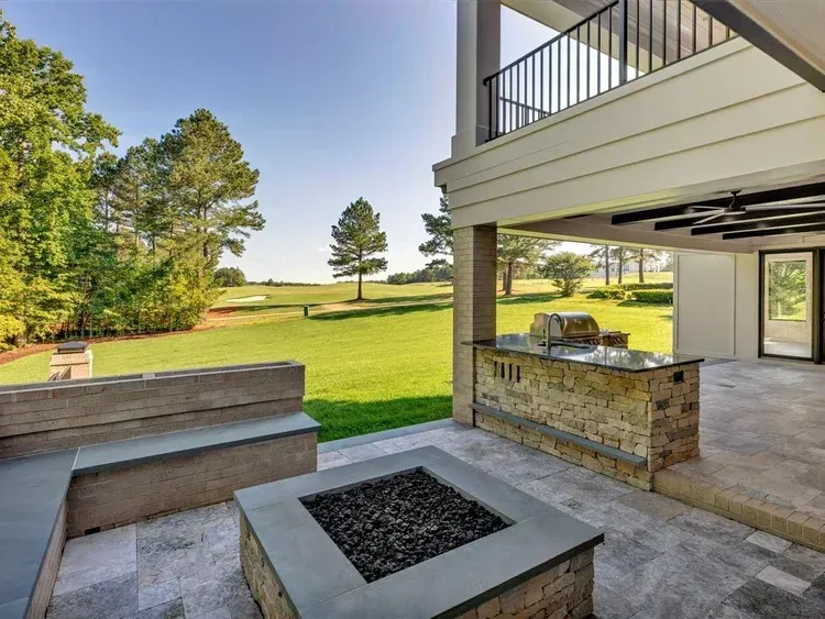 Patio with fire pit and bench seating overlooking a green lawn and trees under a covered deck