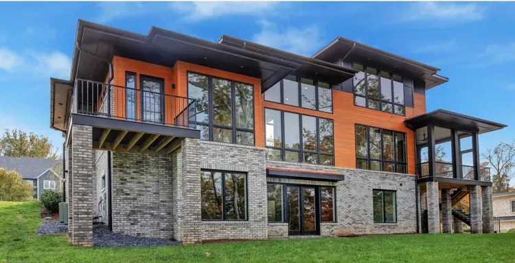 Modern two-story stone and wood house with large windows and balconies on a grassy lot