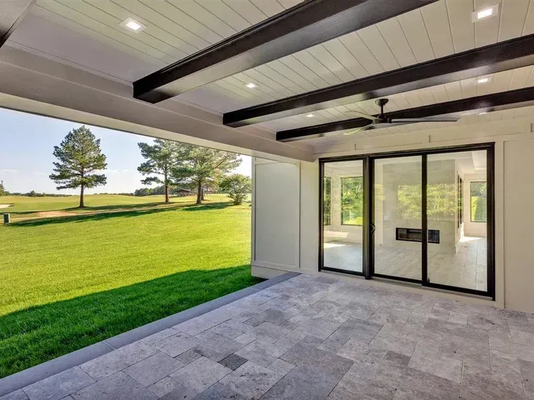 Covered patio with sliding glass doors opening to a green lawn and trees.