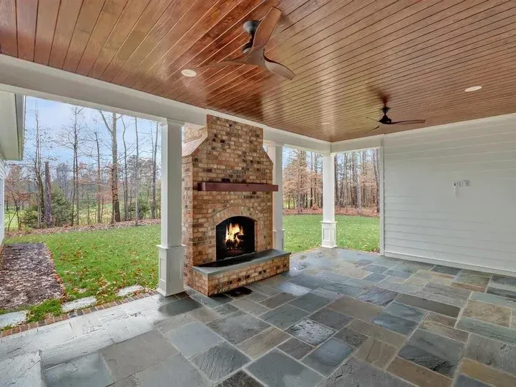 Covered patio with stone fireplace, slate floor, white columns, and wooded backyard view