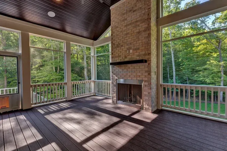 Spacious screened porch with brick fireplace, wood ceiling, and large windows overlooking trees