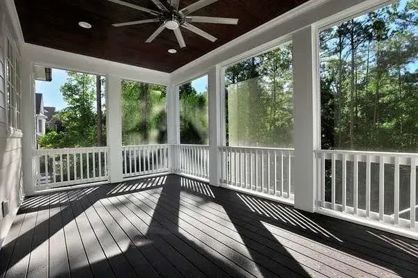 Screened porch with dark wood floor, white railing, and ceiling fan overlooking trees