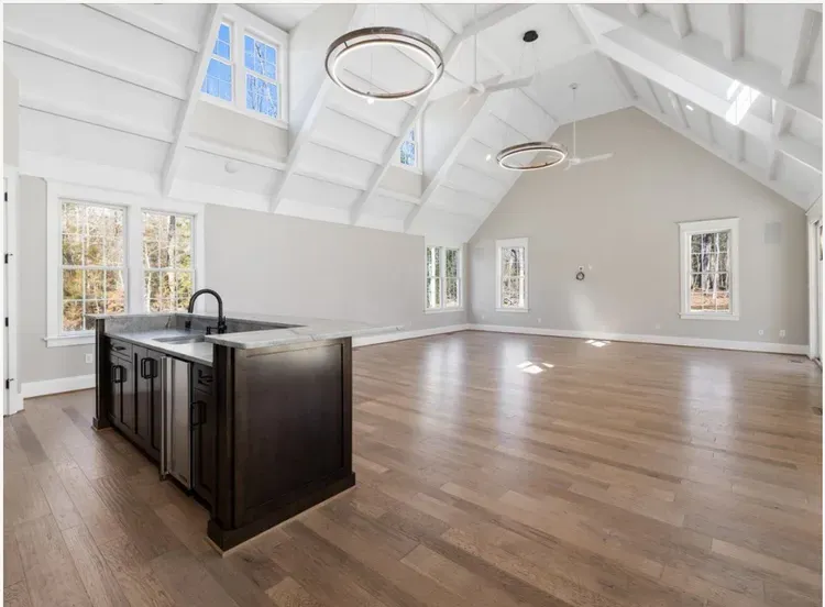 Spacious modern kitchen with vaulted white ceiling, wood floors, and a dark island