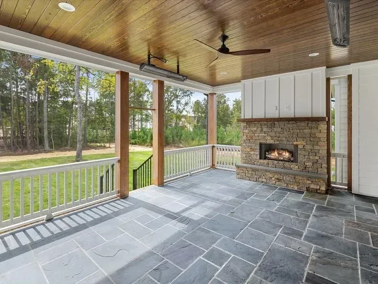 Covered patio with slate floor, wood ceiling, stone fireplace, and view of a grassy yard and trees