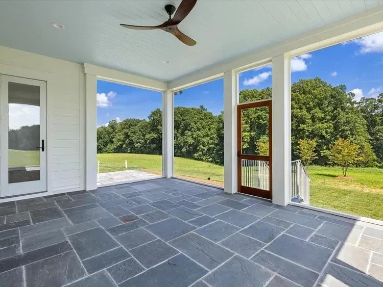 Covered patio with slate floor, ceiling fan, and open views of a green lawn and trees